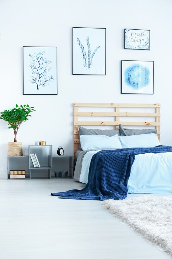 New bedroom with wood bed, blue bedding, posters and plant